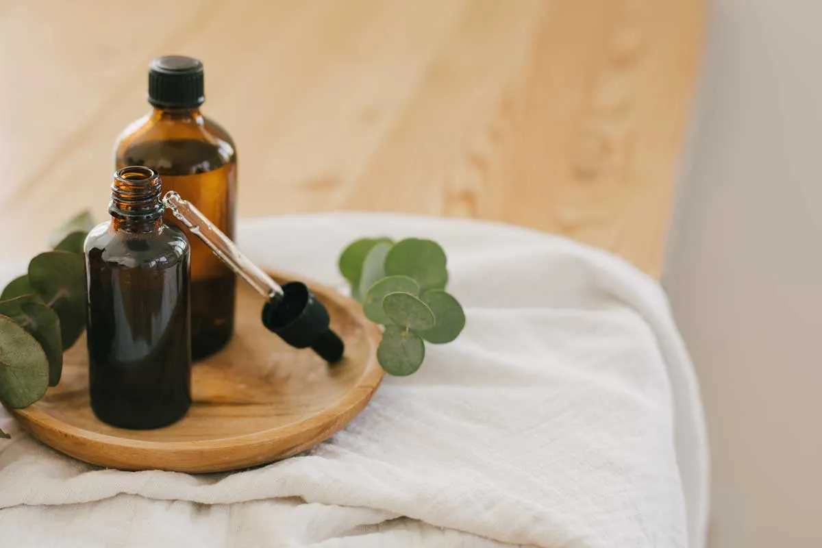 Amber bottles of natural cleaning solution beside eucalyptus sprigs on a folded white towel