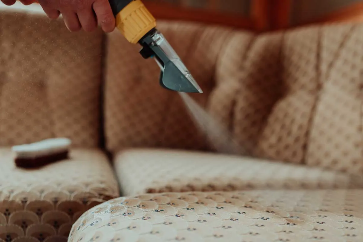An upholstery tool cleaning the cushion of a cream tufted sofa